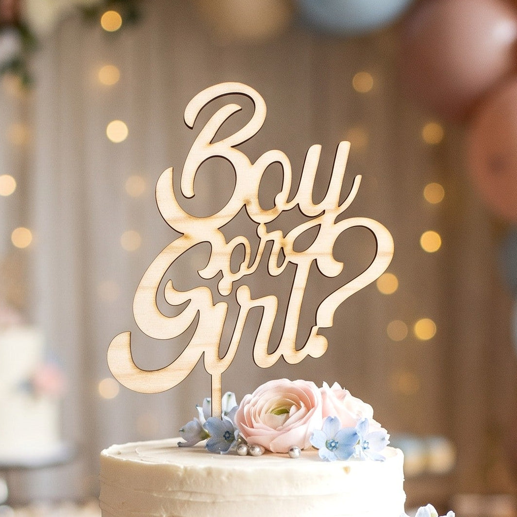 Wooderland wooden Boy or Girl cake topper on a two-tier white frosted cake decorated with pastel flowers