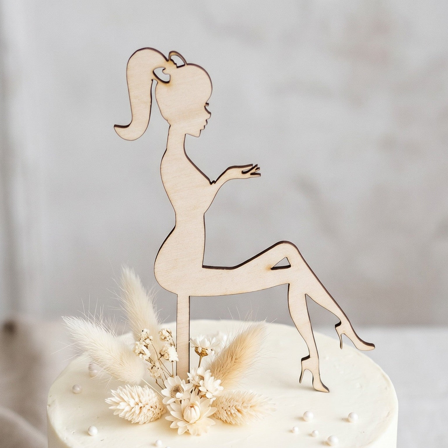 Wooderland bride silhouette wooden cake topper on a white frosted cake with dried flowers.