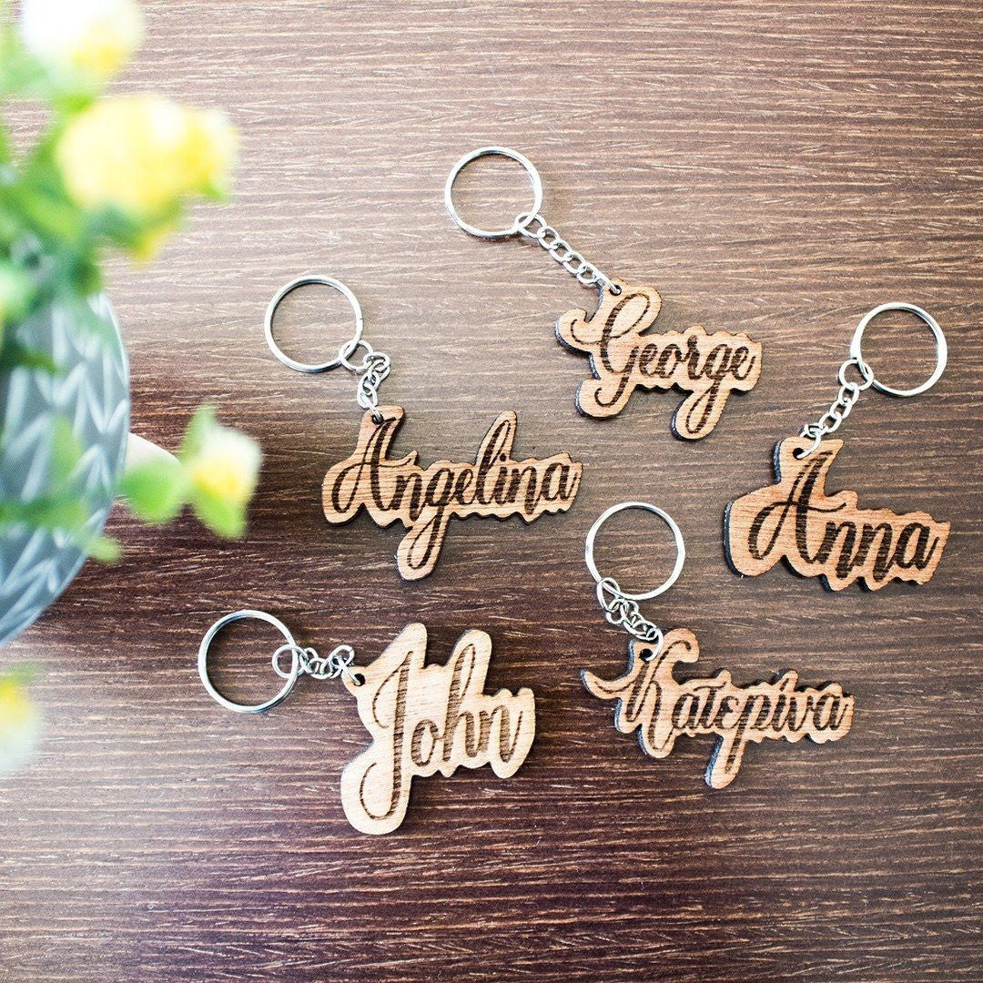 Wooderland custom engraved wooden name keyrings with cursive lettering on a wooden table surface.