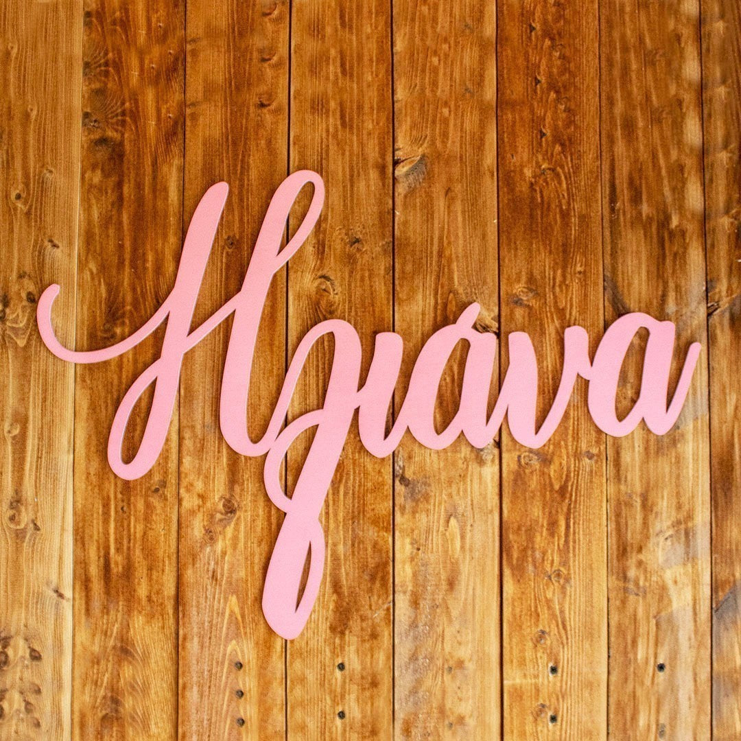 Wooderland custom laser-cut wooden name sign in blush pink script font mounted on a rustic wooden wall backdrop.