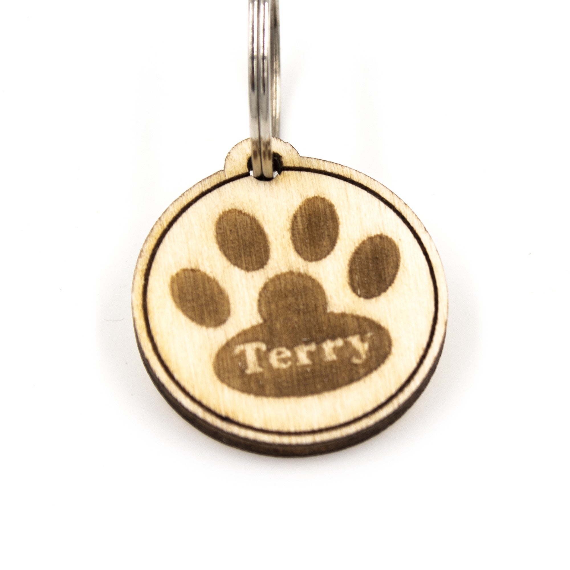 Wooderland custom round wooden dog tag with engraved paw print and the name Terry on a white background
