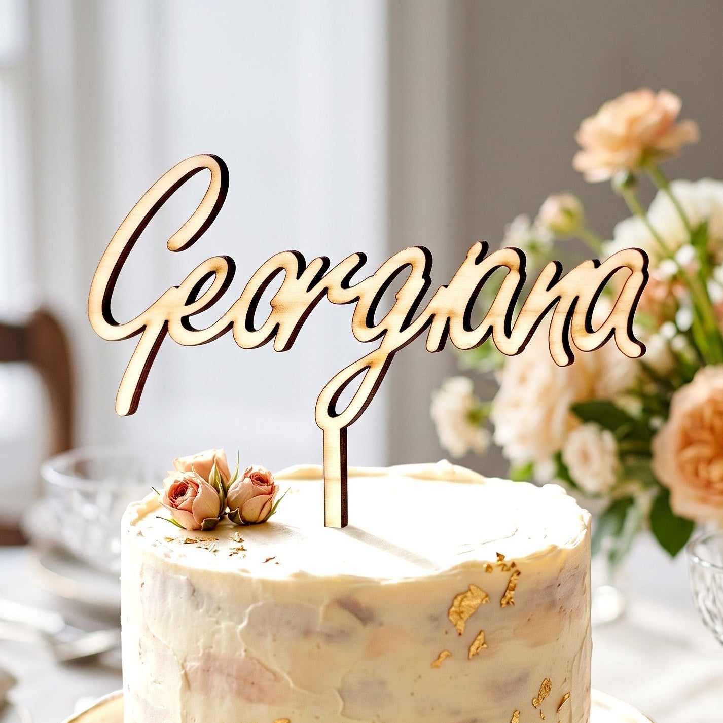 Wooderland custom laser-cut wooden name cake topper featuring elegant cursive script on a frosted cake with gold leaf.