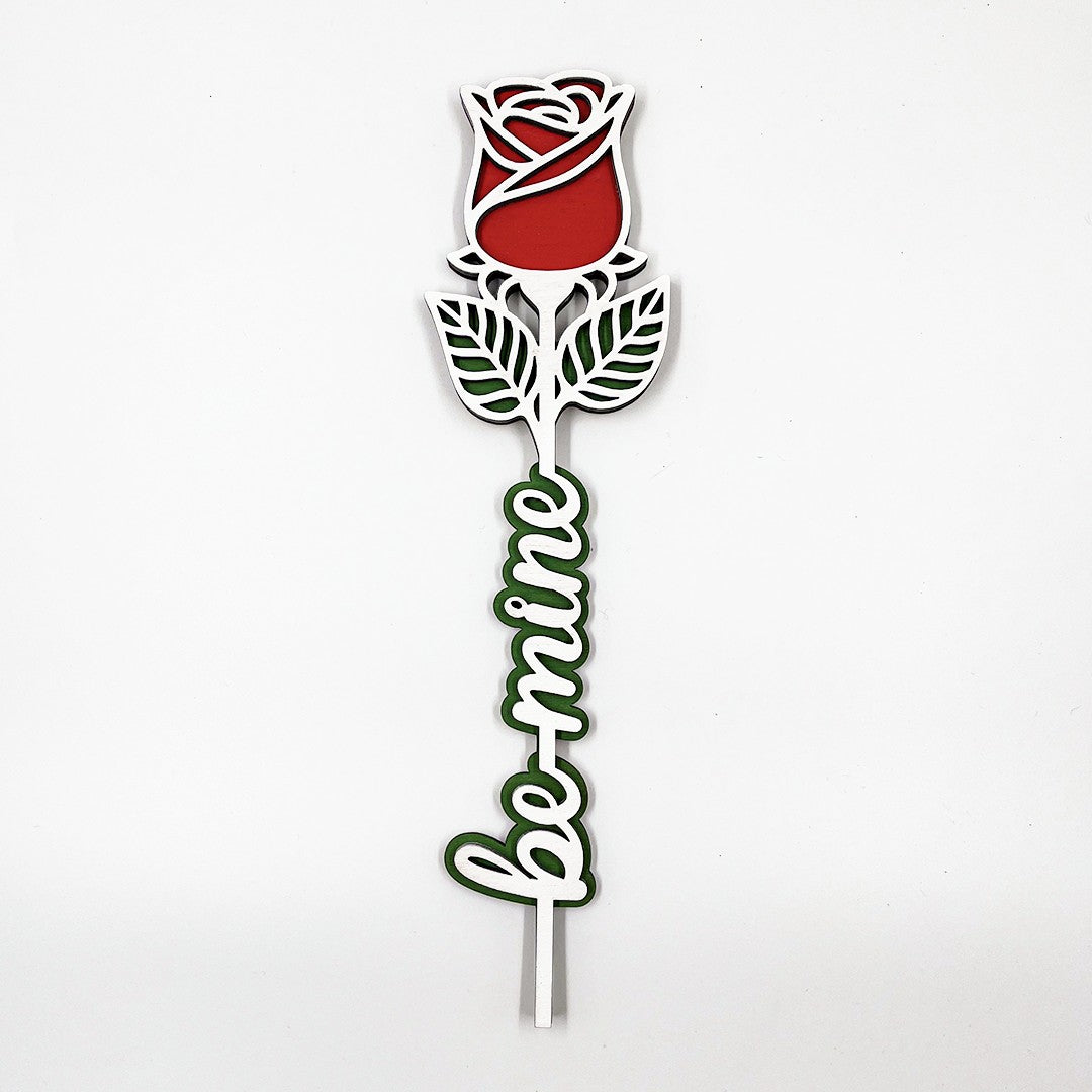 Wooderland engraved wooden rose featuring a red bloom, green leaves, and the text Be Mine in a white script font.