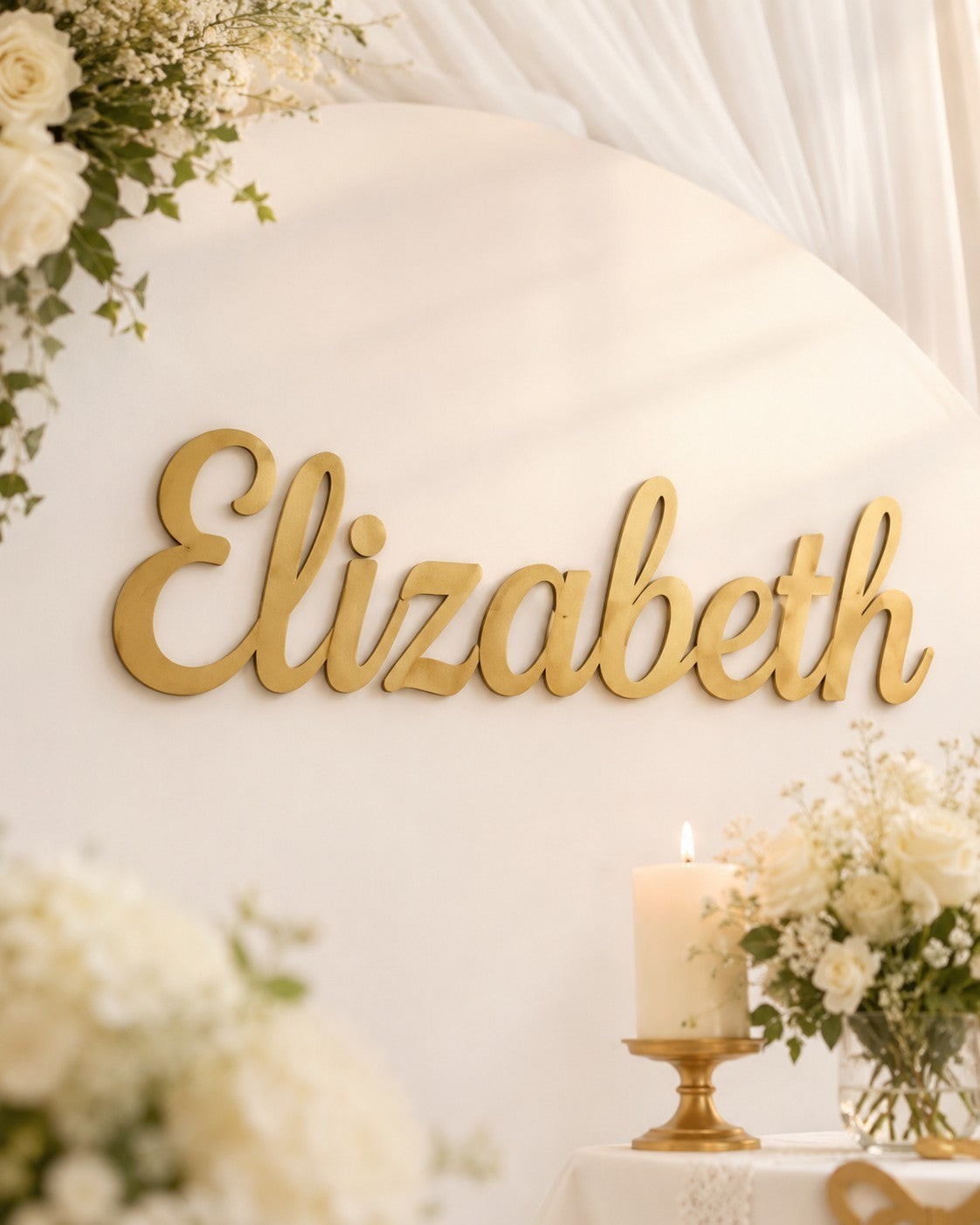 Wooderland gold laser-cut wooden name sign Elizabeth displayed on a white event backdrop with floral arrangements.
