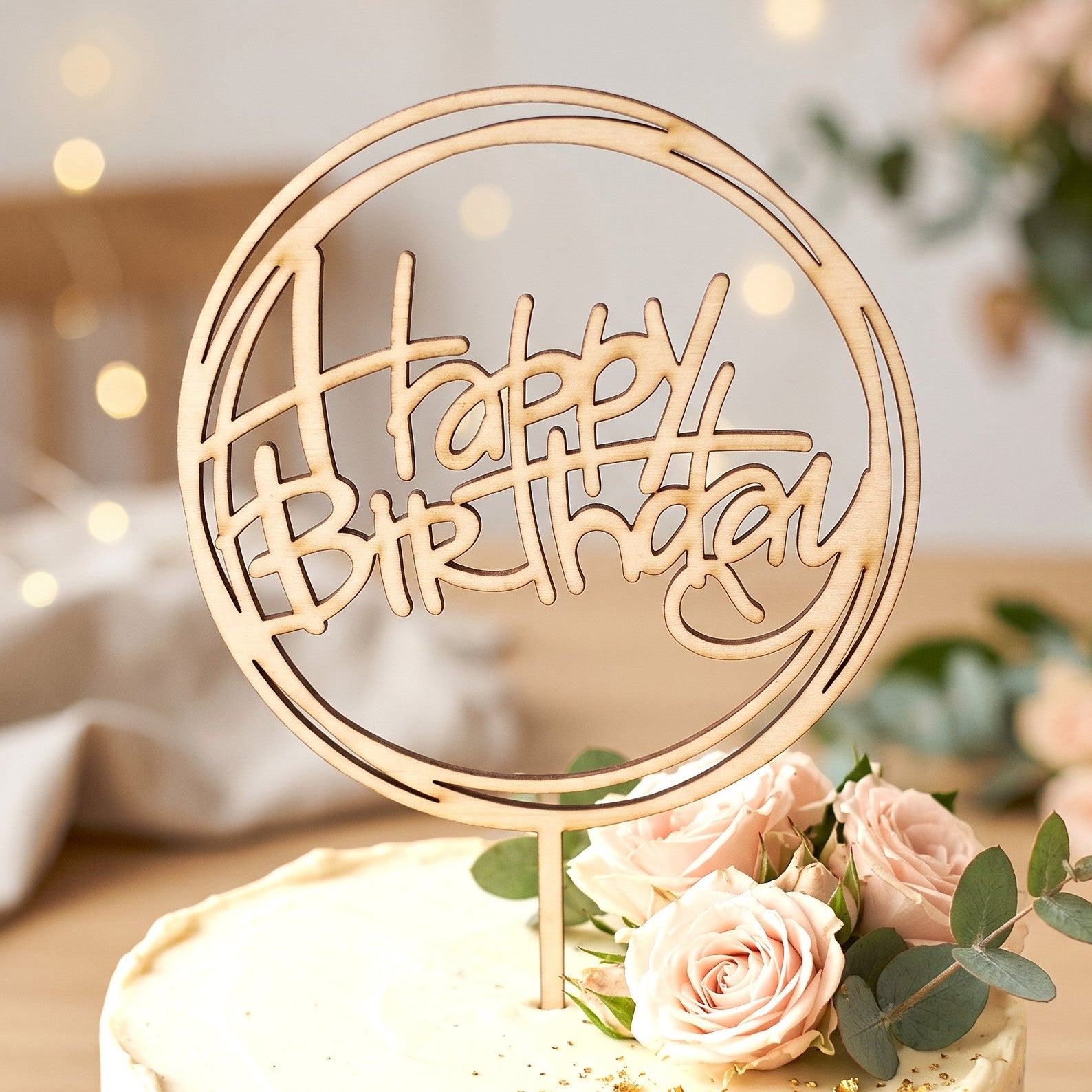 Wooderland laser-cut wooden Happy Birthday cake topper on a frosted cake decorated with soft pink roses.