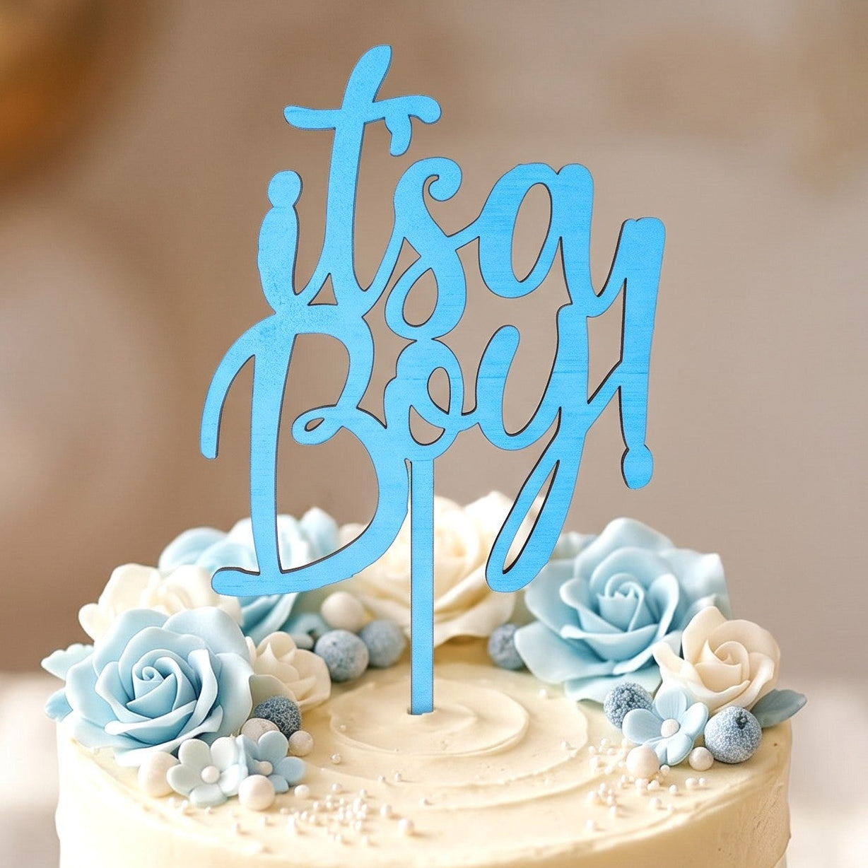 Wooderland blue wooden It's a Boy cake topper on a decorated baby shower cake with blue and white floral frosting.