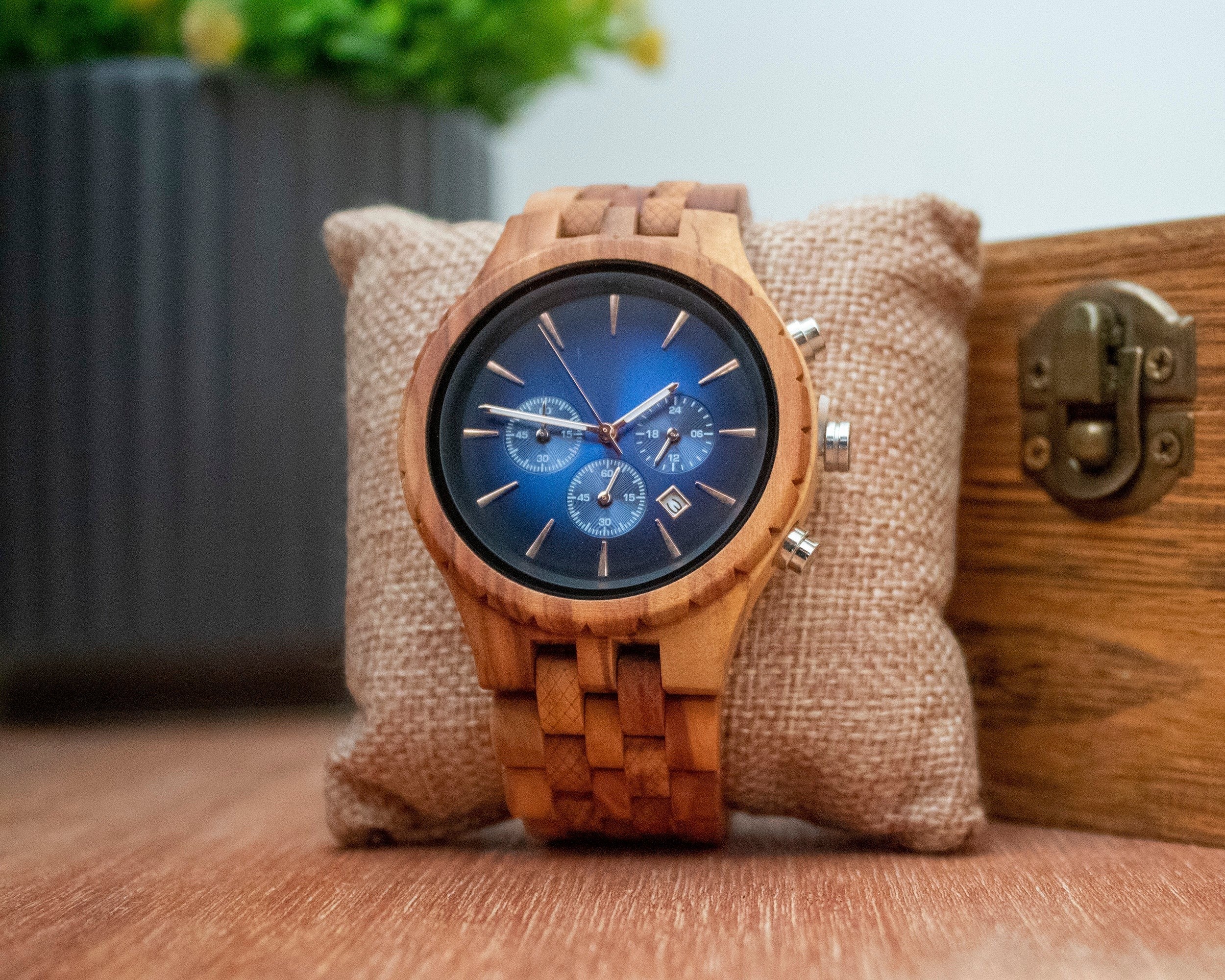 Wooderland Jupiter wooden wristwatch with a blue chronograph dial and natural wood grain band on a burlap cushion.