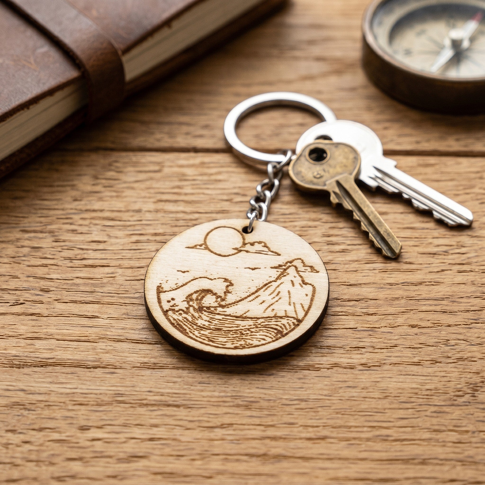 Wooderland round wooden keyring featuring an engraved mountain and ocean wave design on a rustic wooden surface.