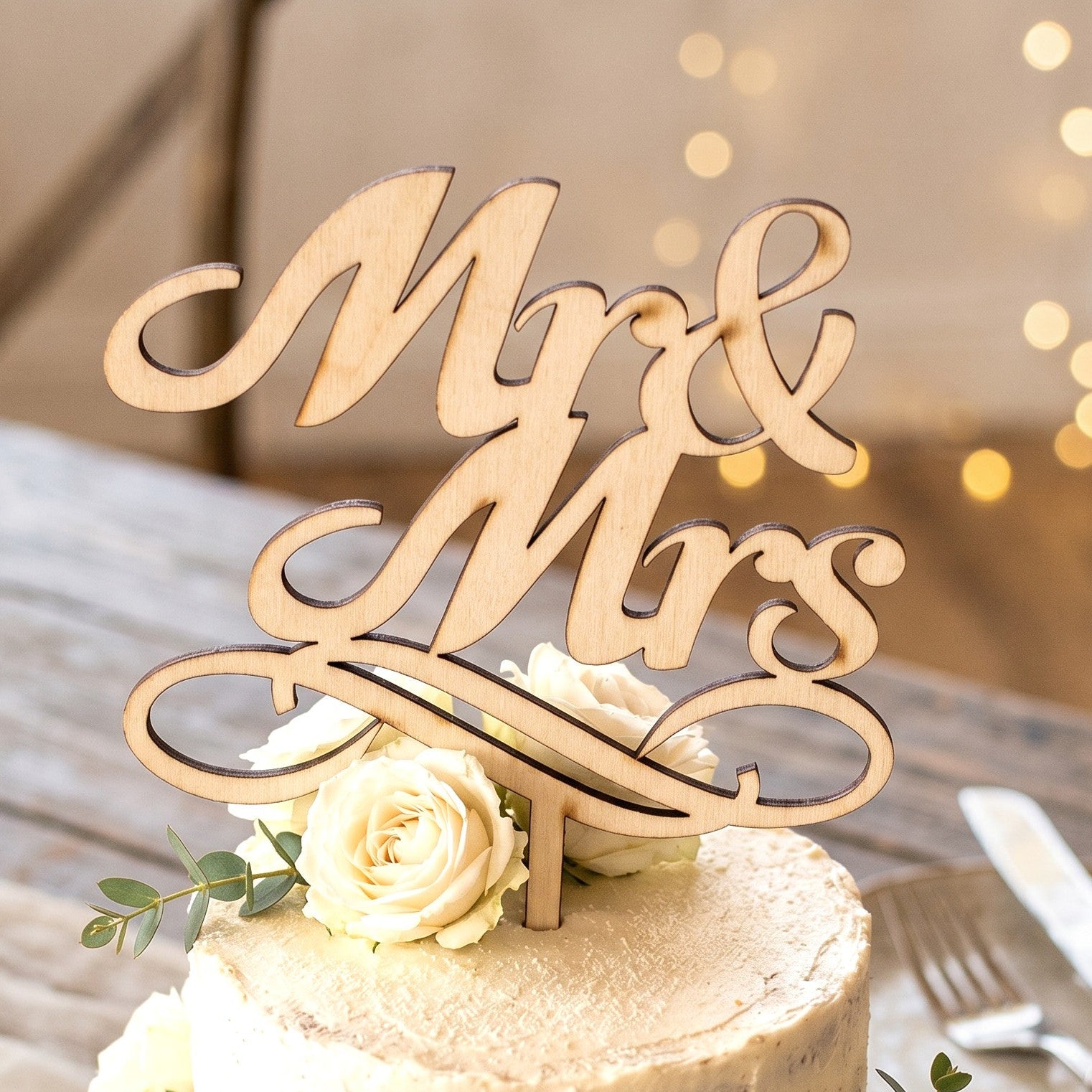 Wooderland laser-cut wooden Mr & Mrs wedding cake topper on a white frosted cake decorated with white roses