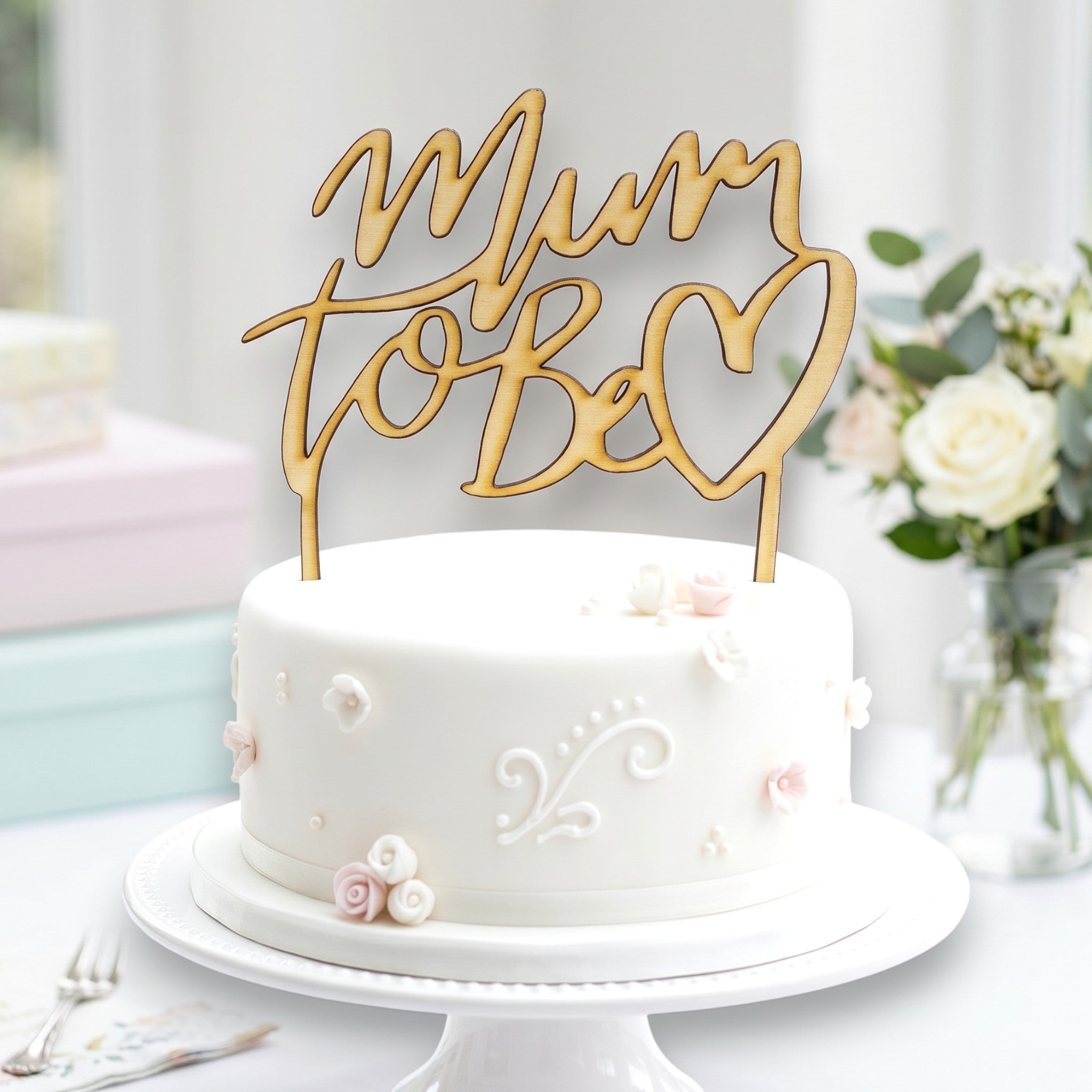 Wooderland Mum to Be wooden cake topper in laser-cut script on a white baby shower cake with floral decorations.