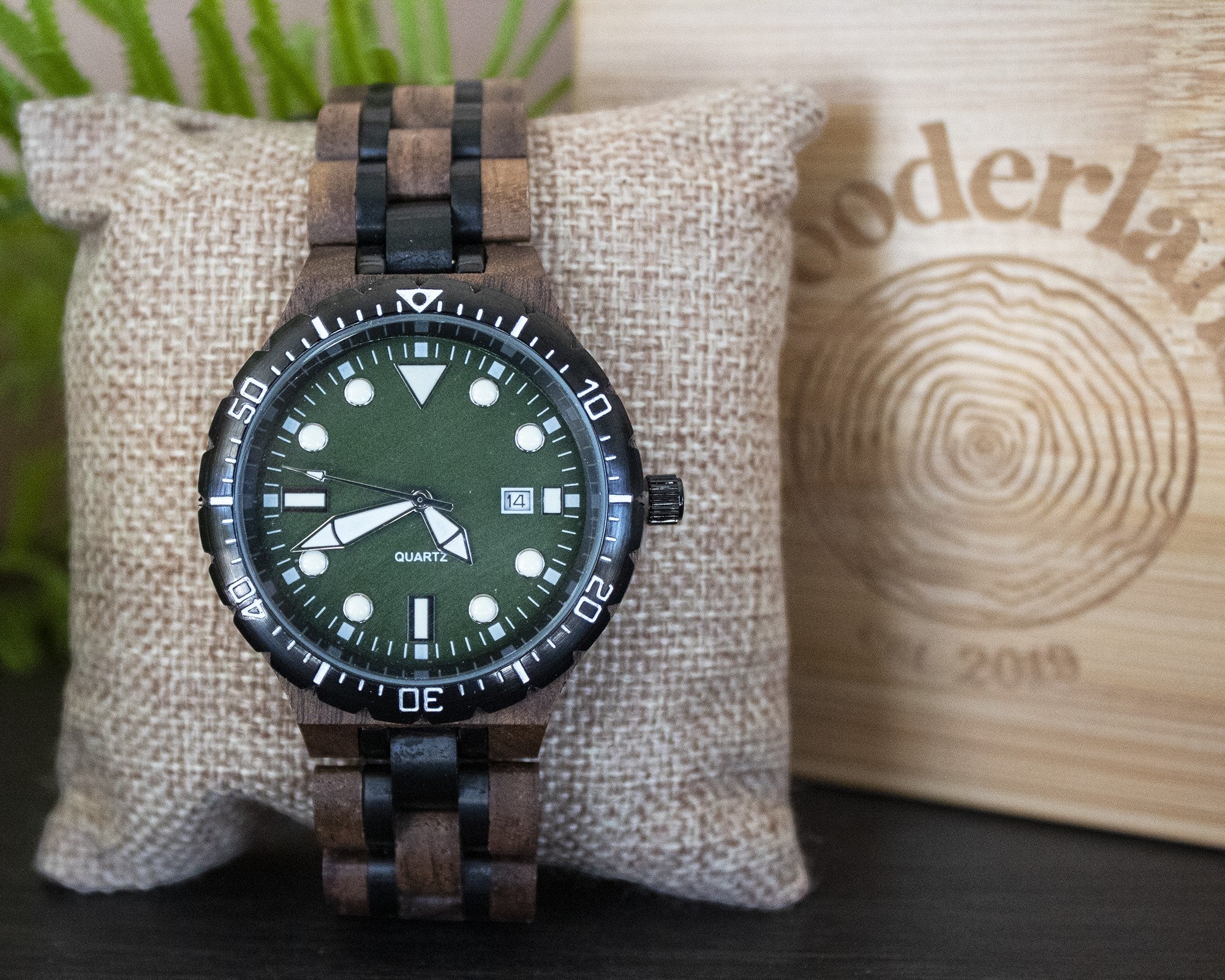 Wooderland Orcus wooden watch with a green dial, black bezel, and dark wood link strap on a textured display pillow.