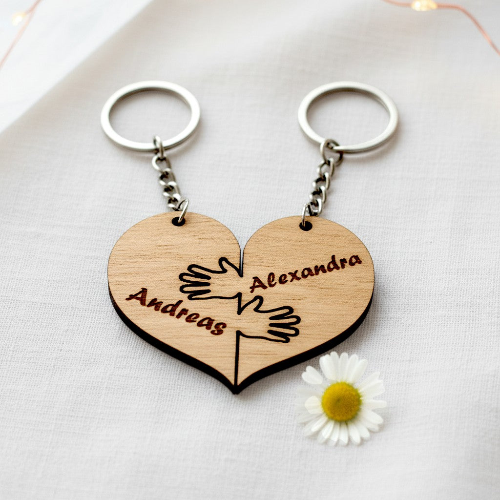 Wooderland matching wooden heart keyrings with engraved names and hand-holding design on a white fabric background