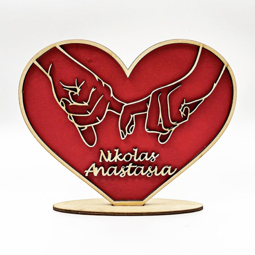Wooderland personalized wooden heart stand featuring carved hands holding pinky fingers, painted red with names.