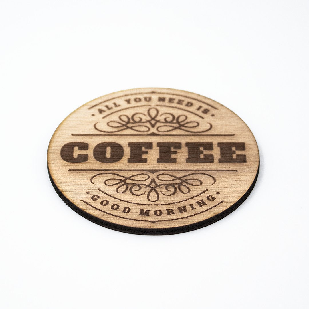 Wooderland round wooden coaster with laser-engraved coffee quote and decorative flourishes on a white background