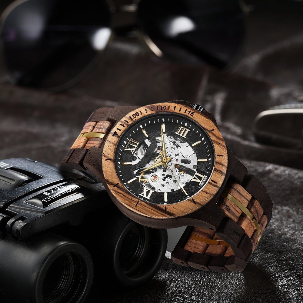 Wooderland Saturn automatic wooden watch with a dark wood band, skeleton dial, and gold accents on a leather surface.