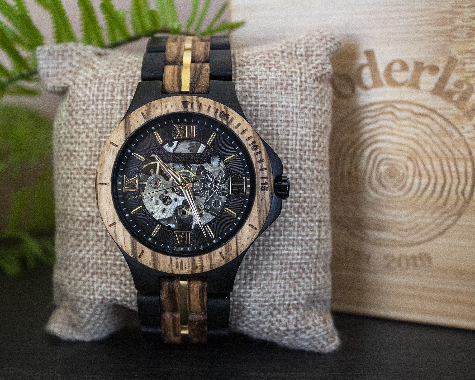 Wooderland Saturn automatic wooden watch with black and natural wood grain finish on a textured display cushion.