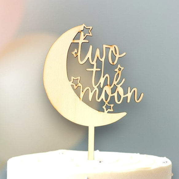 Wooderland wooden Two the Moon cake topper on a white frosted birthday cake with star sprinkles and balloons.