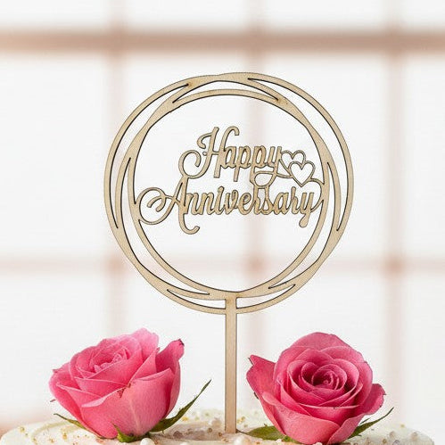Wooderland laser-cut wooden Happy Anniversary cake topper on a white frosted cake decorated with pink roses.