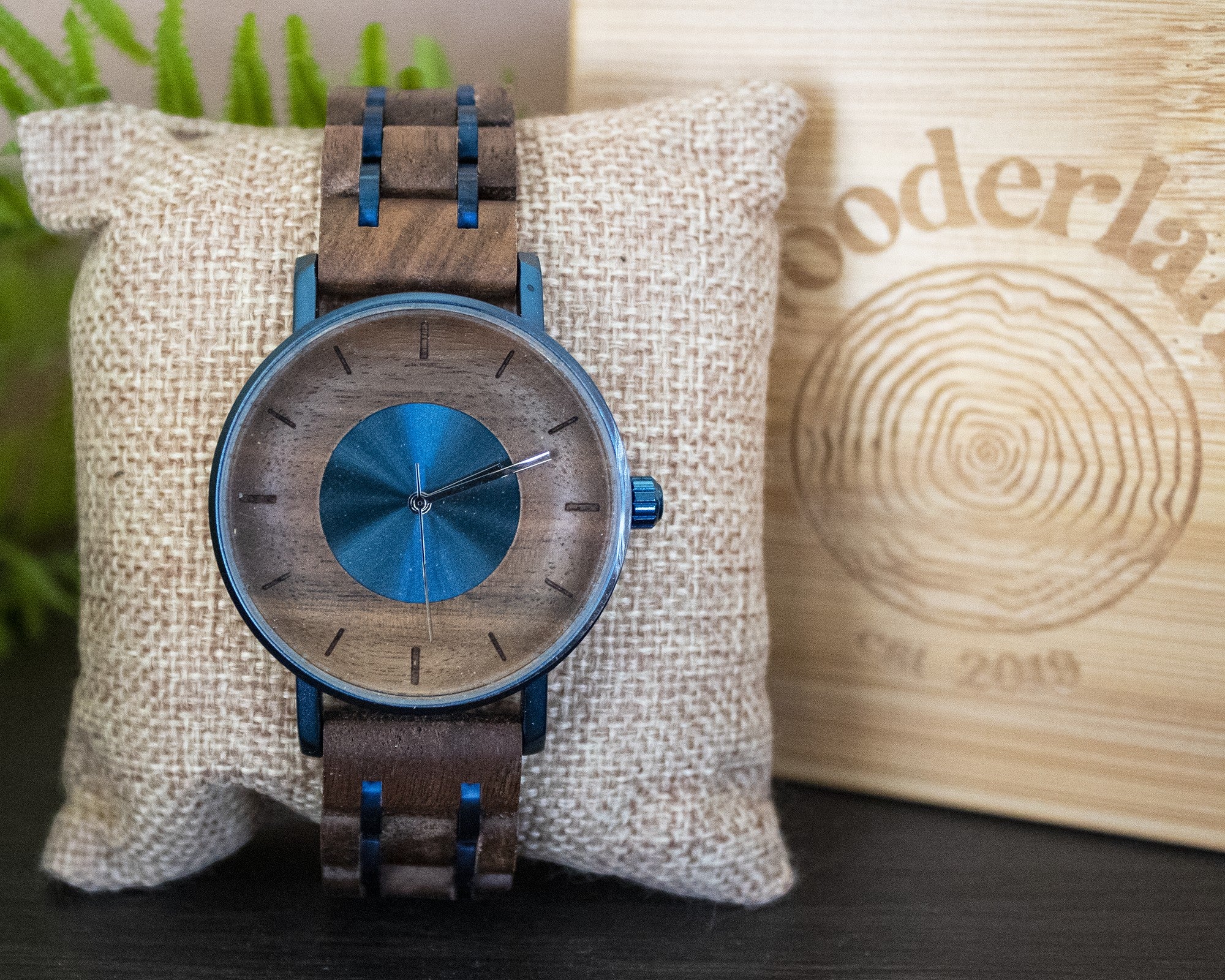Wooderland Earth Watch featuring a dark wood and metallic blue dial with an alloy and wood link strap on a cushion.