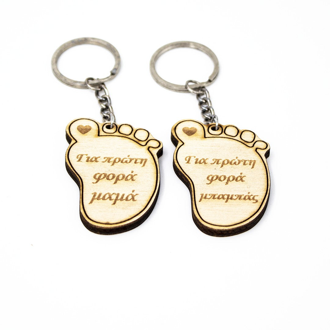 Wooderland wooden foot-shaped keyrings for new parents with engraved Greek text on a white background