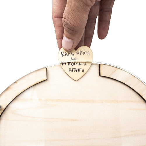 Wooderland wooden heart-shaped guest book frame with a hand placing a small wooden heart inside for wedding wishes.