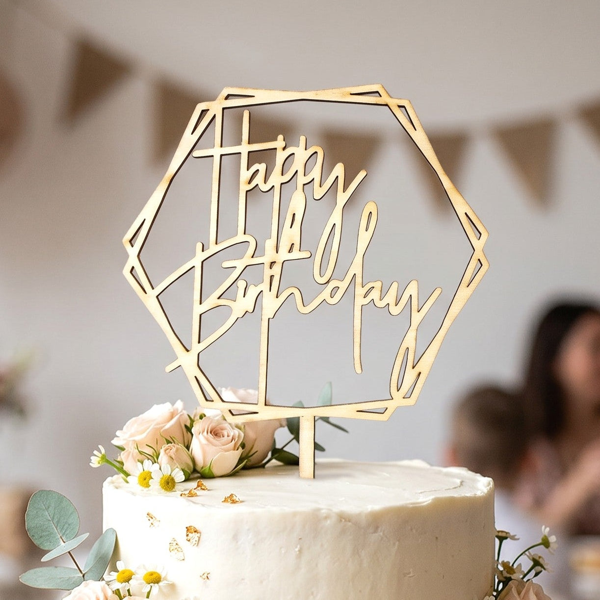 Wooderland laser-cut wooden Happy Birthday cake topper in a hexagon frame on a two-tier white floral birthday cake.