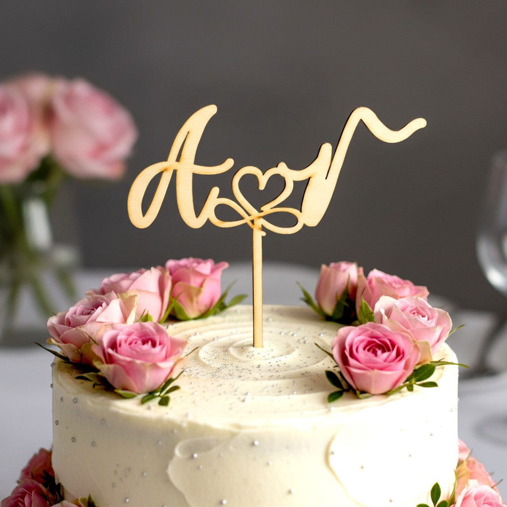 Wooderland wooden cake topper with personalized initials and heart detail on a white wedding cake with pink roses.