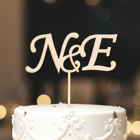 Wooderland custom wooden two-initial monogram cake topper on a white tiered wedding cake with roses.