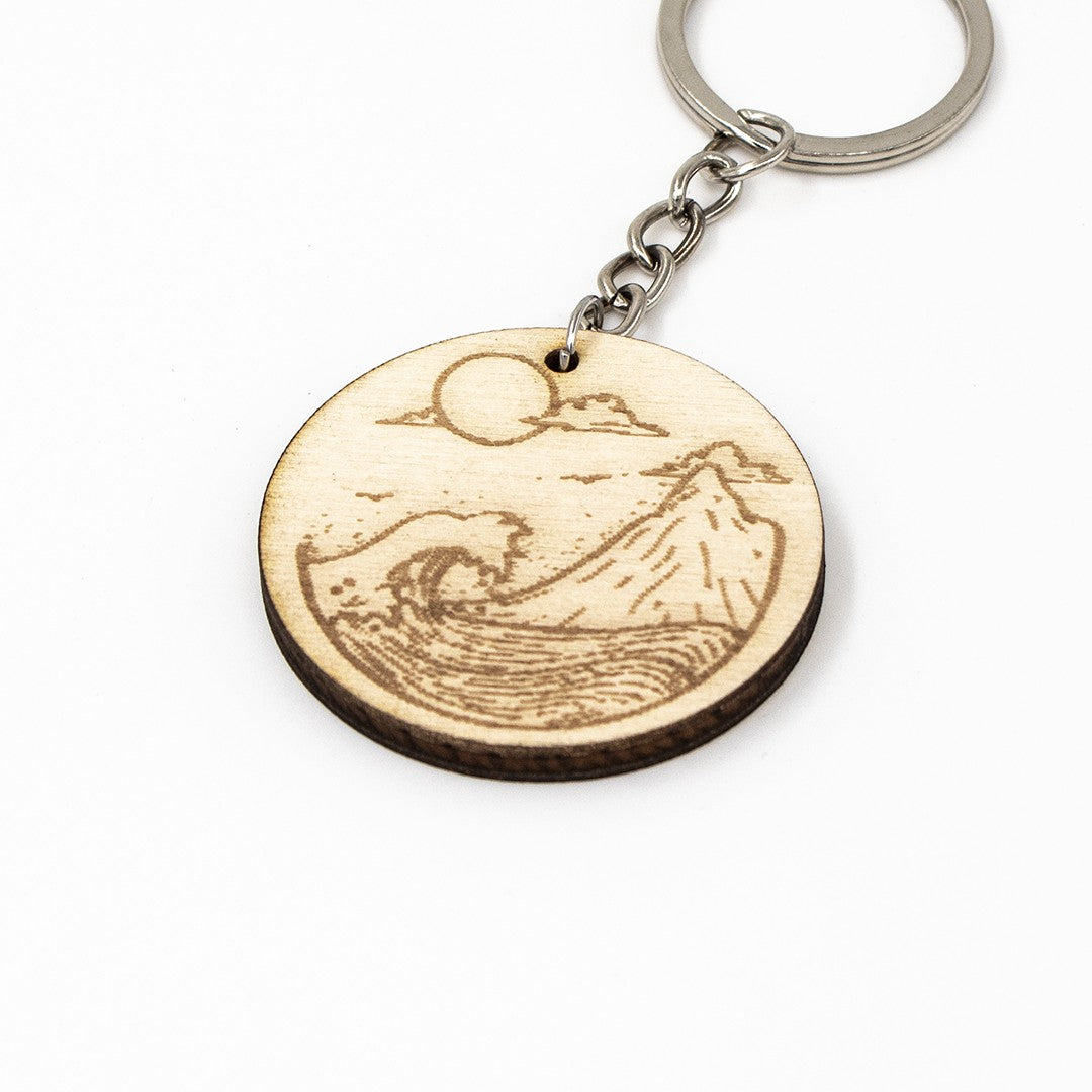 Wooderland round wooden keyring featuring a laser-engraved mountain and ocean wave design on a metal key ring.