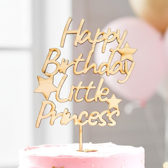 Wooderland laser-cut wooden Happy Birthday Little Princess cake topper on a pink frosted cake with gold star accents.