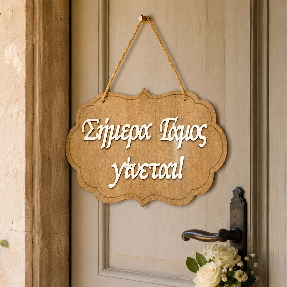 Wooderland wooden wedding welcome sign with white laser-cut Greek text hanging on a door with a floral accent.